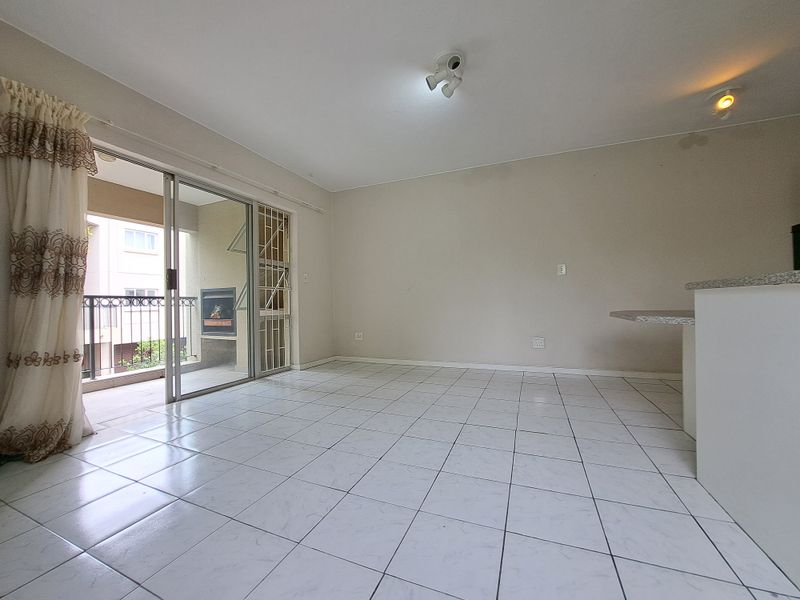 Spacious open-plan living area featuring neutral tiled flooring, a breakfast counter, and large sliding doors leading to a private balcony.