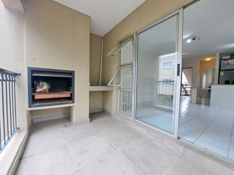 Covered balcony featuring a built-in braai, tiled flooring, and sliding glass doors providing access to the interior living area.