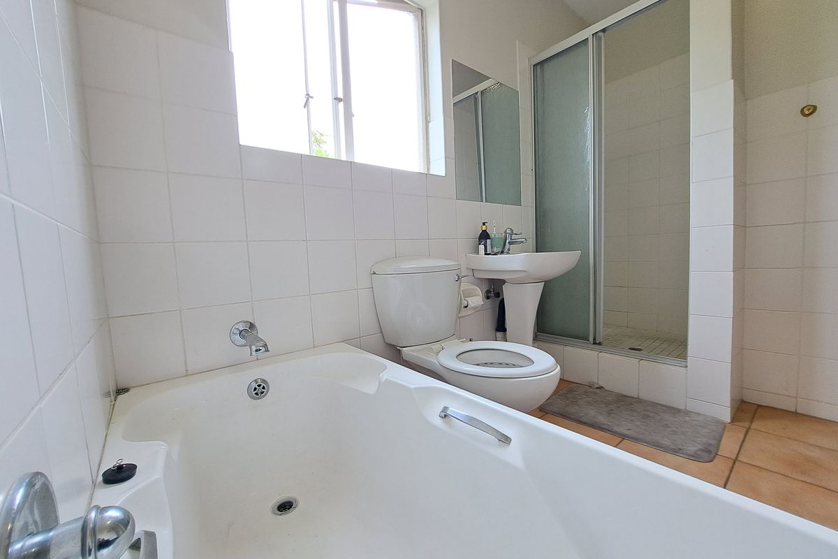 A functional bathroom featuring a bathtub, separate shower enclosure, pedestal basin, and toilet with neutral wall and floor tiling.