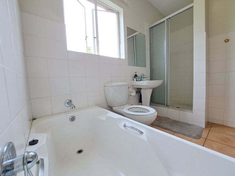 A functional bathroom featuring a bathtub, separate shower enclosure, pedestal basin, and toilet with neutral wall and floor tiling.