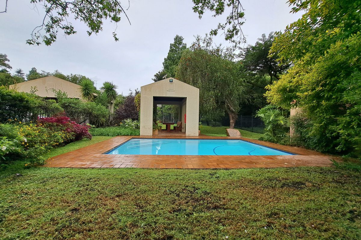 A well-maintained swimming pool area featuring a brick surround and a covered gazebo, set within a lush, landscaped garden environment.