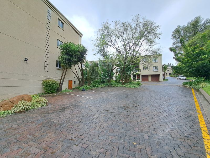 Exterior view of the apartment complex featuring a paved driveway, designated parking bays, and established garden landscaping.