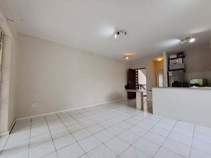 An open-plan living and kitchen area featuring tiled flooring, a breakfast counter, and neutral wall finishes, offering a versatile space for customization.