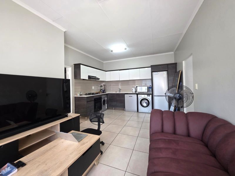 Open-plan living area featuring a modern kitchen with built-in cabinetry, tiled flooring, and integrated appliances, seamlessly flowing into the lounge space.
