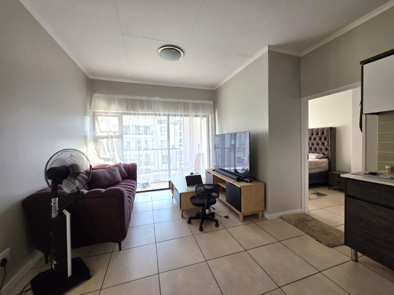 Open-plan living area featuring tiled flooring and a sliding glass door leading to a balcony, with an adjacent kitchen and bedroom access.