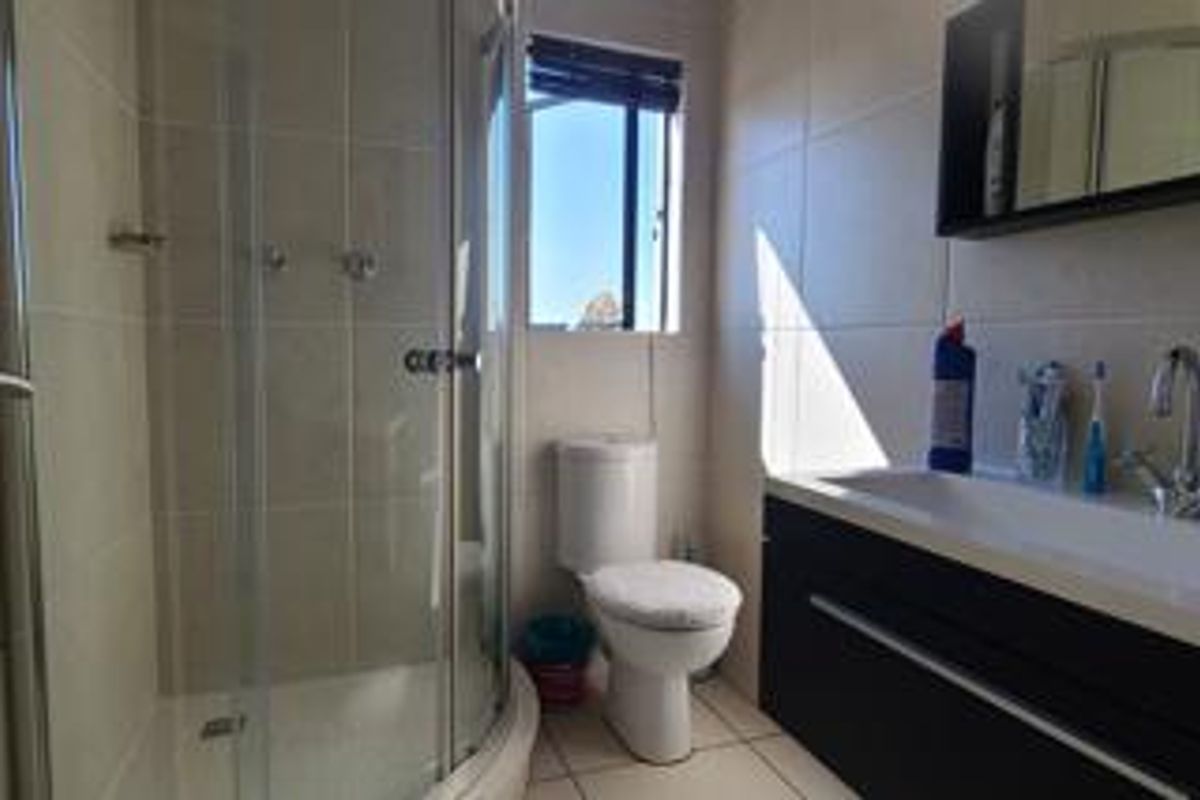 A functional bathroom featuring a corner shower enclosure, a modern vanity with basin, and neutral wall and floor tiling.