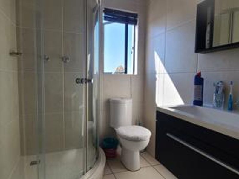 A functional bathroom featuring a corner shower enclosure, a modern vanity with basin, and neutral wall and floor tiling.