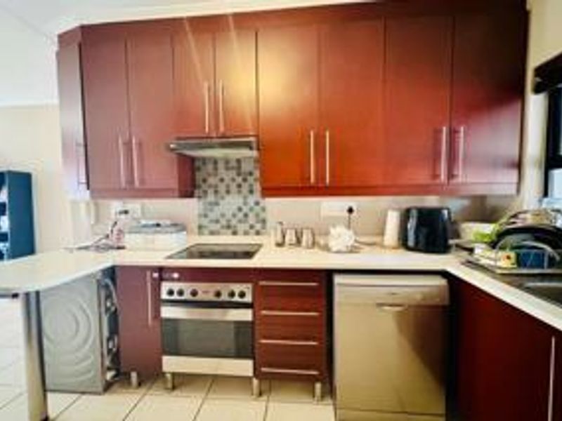 A functional kitchen featuring dark wood cabinetry, a mosaic tile backsplash, built-in oven and hob, and ample counter space for meal preparation.