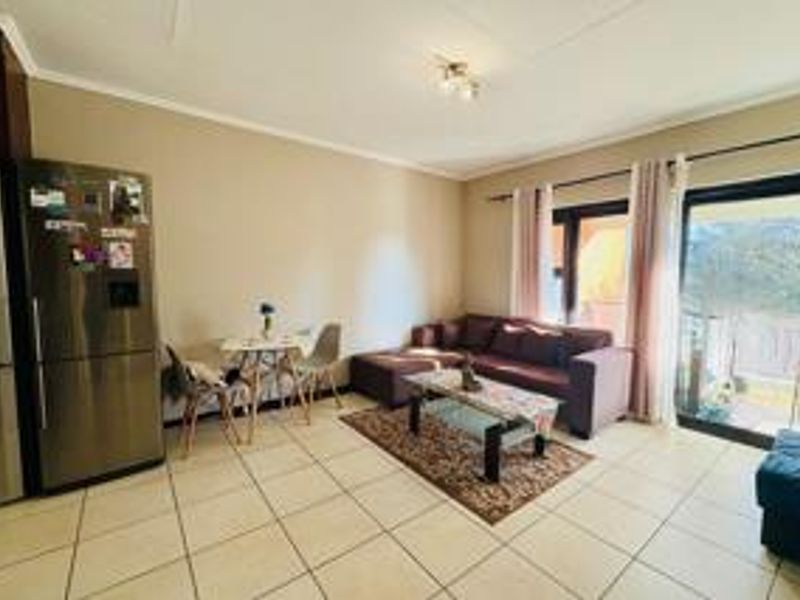 An open-plan living area featuring tiled flooring, neutral wall tones, and a sliding glass door providing access to an outdoor balcony space.