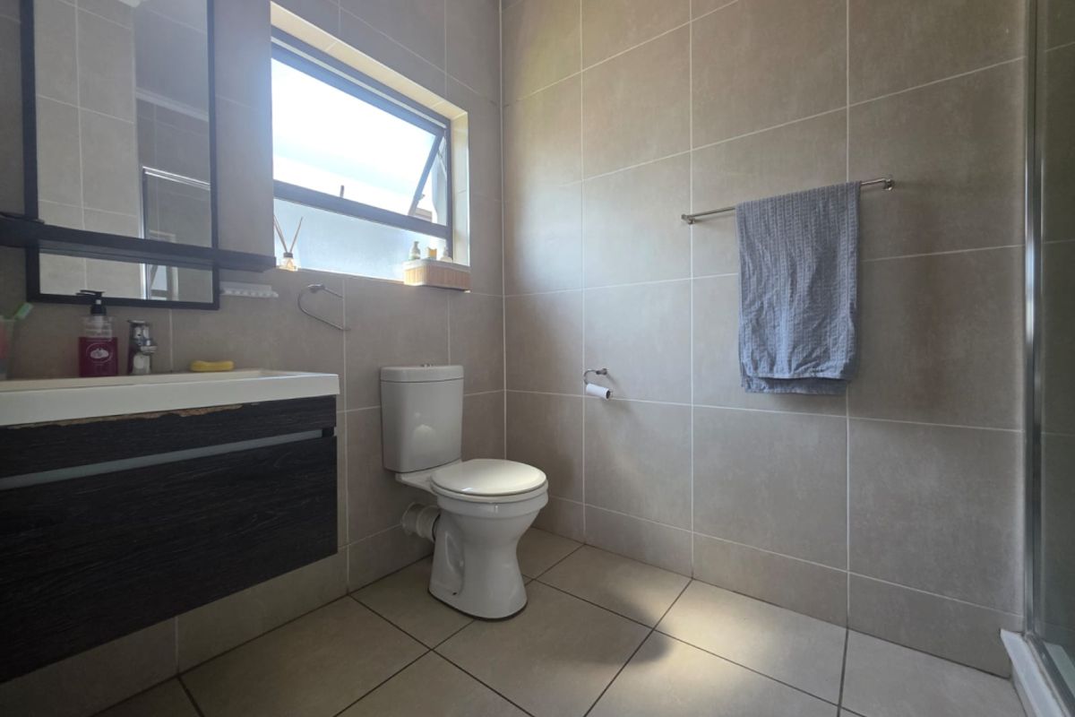 A functional bathroom featuring a vanity unit, toilet, and shower enclosure with neutral wall and floor tiling.