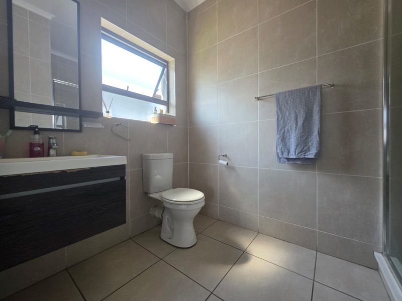 A functional bathroom featuring a vanity unit, toilet, and shower enclosure with neutral wall and floor tiling.