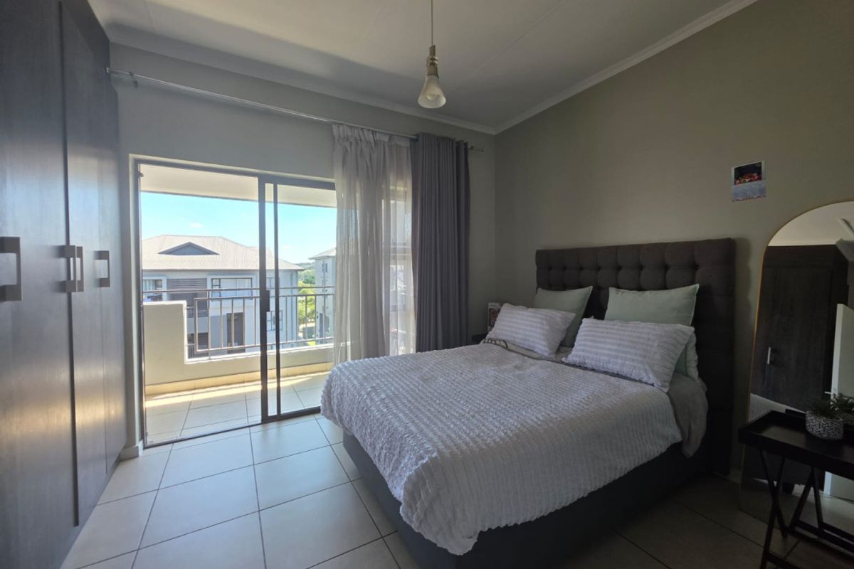 A well-maintained bedroom featuring tiled flooring, built-in cupboards, and a sliding glass door providing direct access to a private balcony.