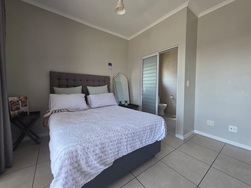 A well-maintained bedroom featuring neutral wall tones, tiled flooring, and direct access to an en-suite bathroom through a sliding door.