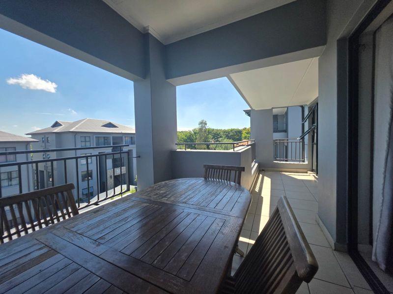 A spacious covered balcony featuring tiled flooring and metal balustrades, offering an open-air outdoor living space.