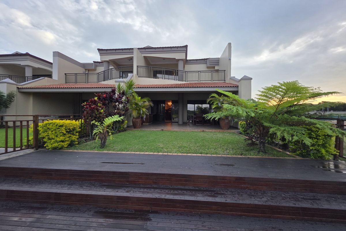Rear view of the apartment featuring a timber deck, landscaped garden, and a covered patio area with upper-level balcony access.