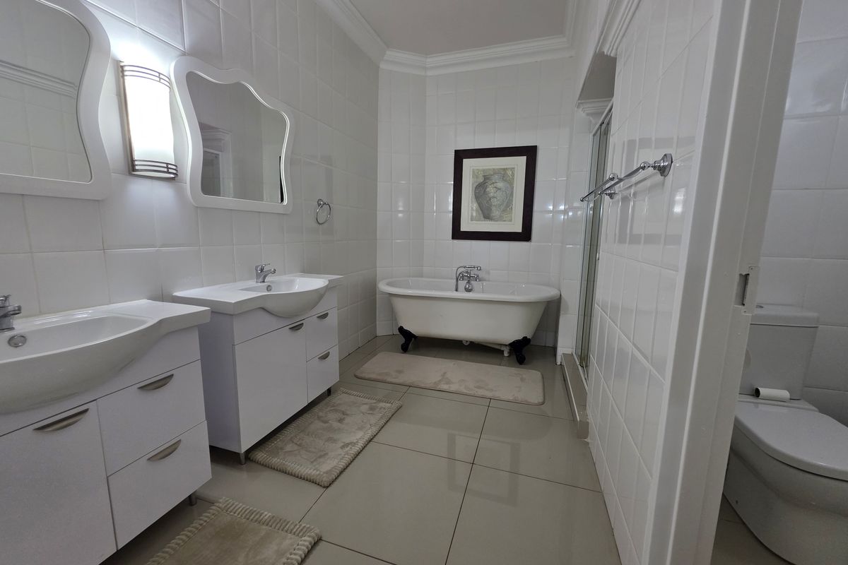 A spacious, well-maintained bathroom featuring a double vanity, a classic freestanding clawfoot bathtub, a separate shower enclosure, and neutral floor-to-ceiling tiling.
