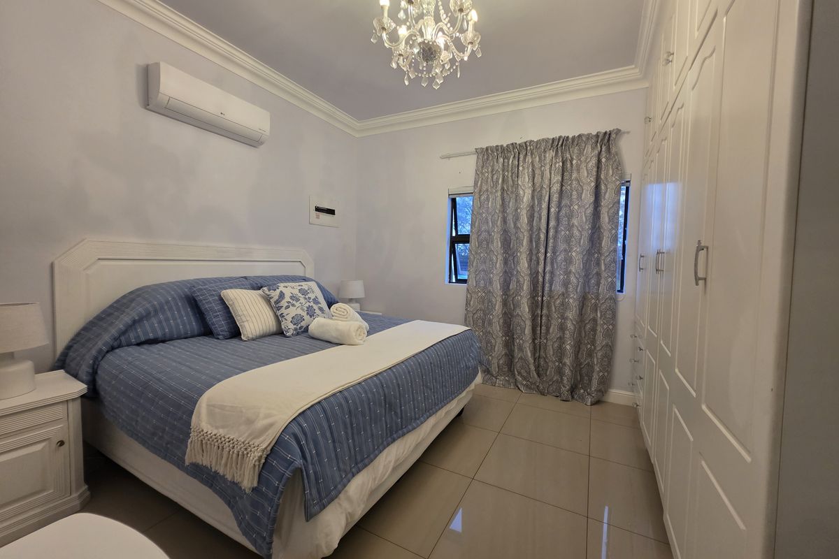 A well-maintained bedroom featuring built-in cupboards, tiled flooring, a split-system air conditioner, and elegant crown molding with a central chandelier.