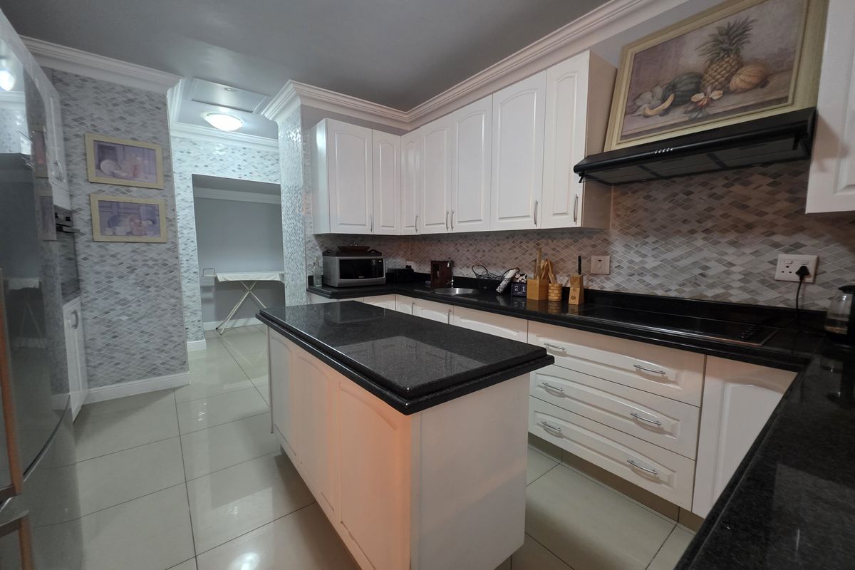 Modern kitchen featuring white cabinetry, contrasting black granite countertops, a central island, and a stylish mosaic tile backsplash with integrated extractor fan.