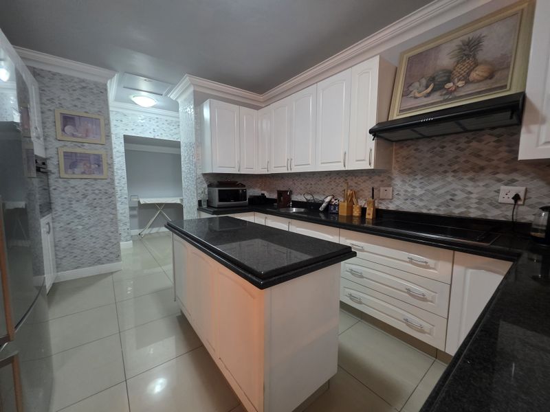 Modern kitchen featuring white cabinetry, contrasting black granite countertops, a central island, and a stylish mosaic tile backsplash with integrated extractor fan.