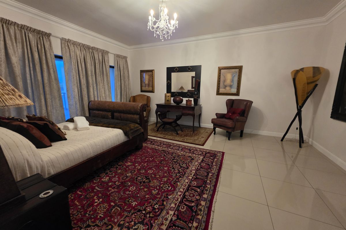 Spacious bedroom featuring polished tile flooring, crown molding, and an elegant crystal chandelier with a decorative ceiling rose.