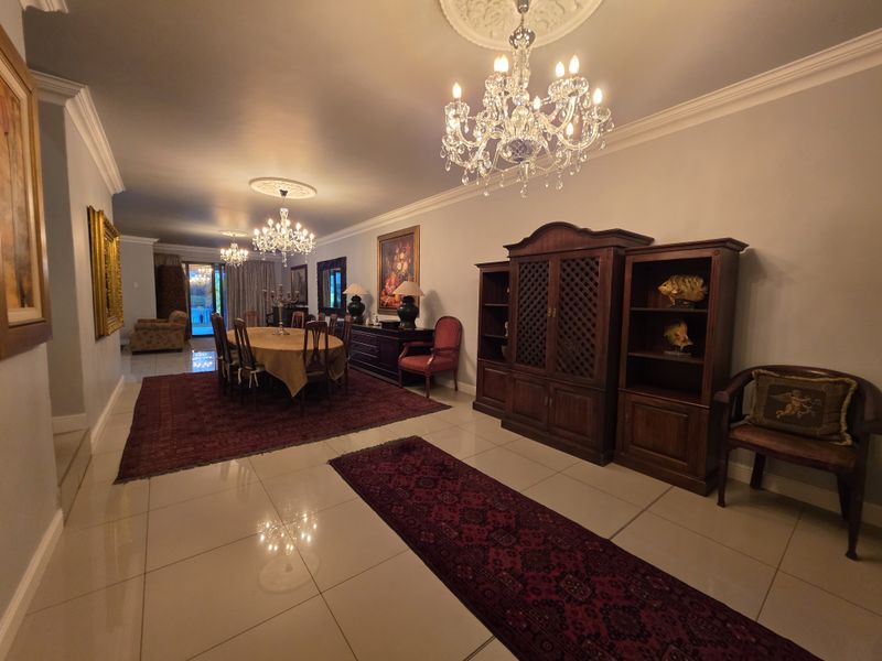 Spacious dining area featuring polished tiled flooring, decorative ceiling roses, and elegant crystal chandeliers, creating a formal and well-maintained atmosphere.