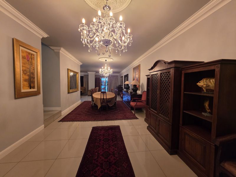 Elegant dining area featuring polished tile flooring, ornate crown molding, and dual crystal chandeliers, creating a sophisticated atmosphere for formal entertaining.