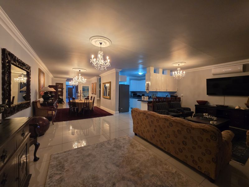 Spacious open-plan living and dining area featuring polished floor tiles, elegant crystal chandeliers, and a modern kitchen with integrated cabinetry.