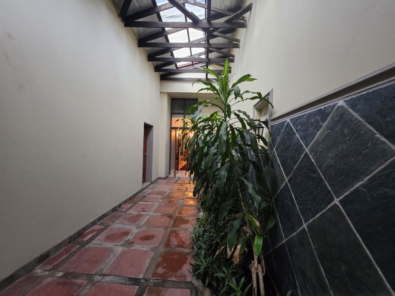 A bright, covered hallway featuring terracotta flooring, slate wall accents, and a skylight with exposed timber trusses, creating a unique transitional space.