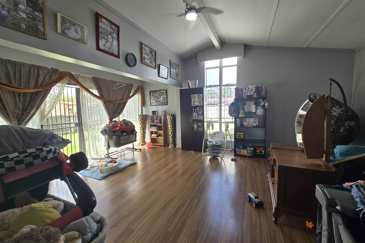 Spacious living room featuring vaulted ceilings, a ceiling fan, and large windows that provide ample natural light, finished with durable laminate flooring.