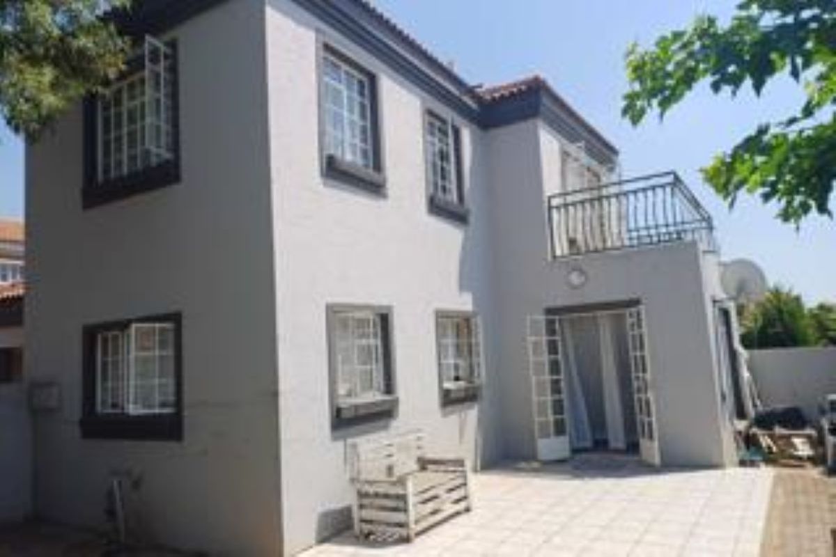 Rear view of a two-story townhouse featuring a tiled patio, upper-level balcony, and classic casement windows with dark trim.