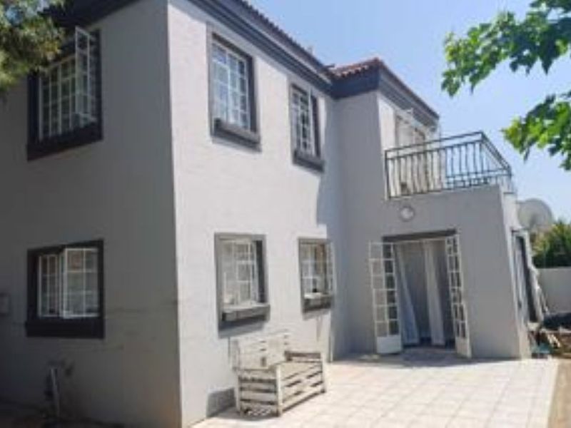 Rear view of a two-story townhouse featuring a tiled patio, upper-level balcony, and classic casement windows with dark trim.