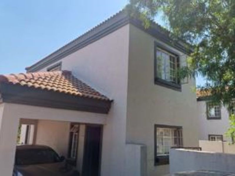 A view of the front exterior of the townhouse, featuring a tiled roof, plastered facade, and an integrated carport.