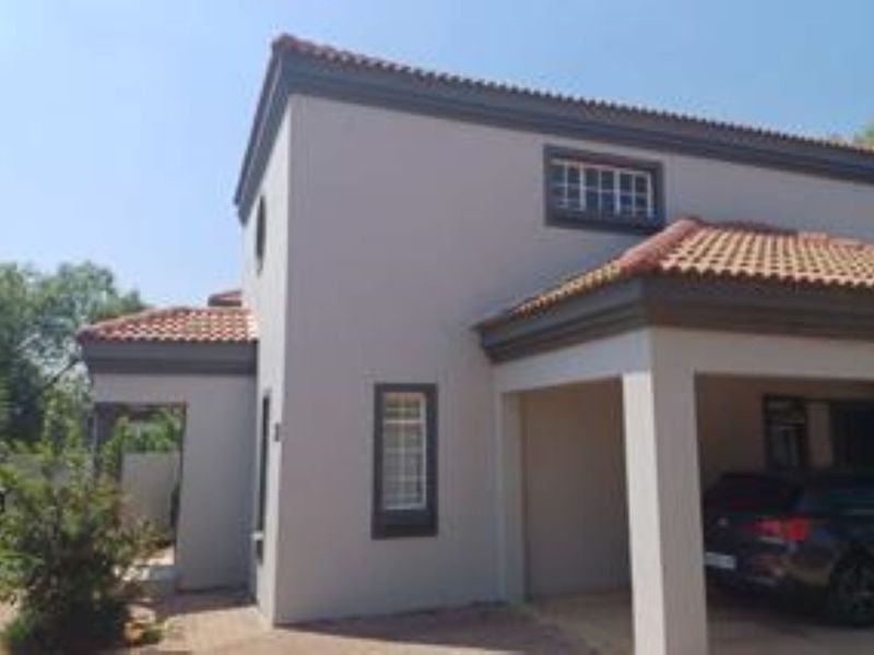 Front elevation of a townhouse featuring a covered carport, terracotta roof tiles, and paved driveway access.