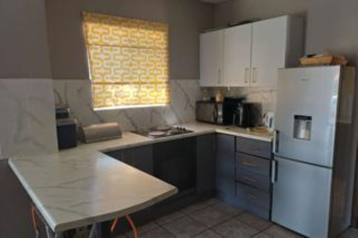 Compact kitchen featuring modern two-tone cabinetry, marble-look countertops, built-in oven, and electric hob with a tiled backsplash.