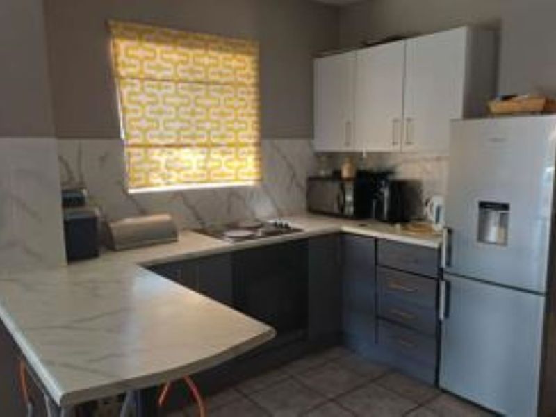 Compact kitchen featuring modern two-tone cabinetry, marble-look countertops, built-in oven, and electric hob with a tiled backsplash.