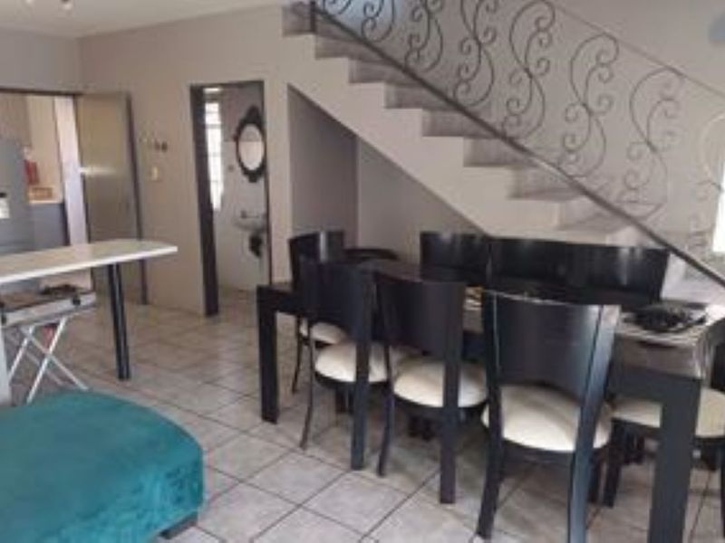 Open plan living and dining area featuring tiled flooring and a decorative wrought iron staircase railing, with an adjacent kitchen and guest bathroom.