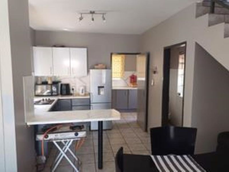 Open plan kitchen area featuring built-in cabinetry, a breakfast bar, and tiled flooring, with an adjacent scullery and staircase access.