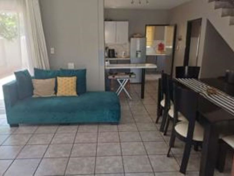 Open plan living and dining area featuring tiled flooring and an adjacent kitchen with breakfast bar, leading to an outdoor patio area.