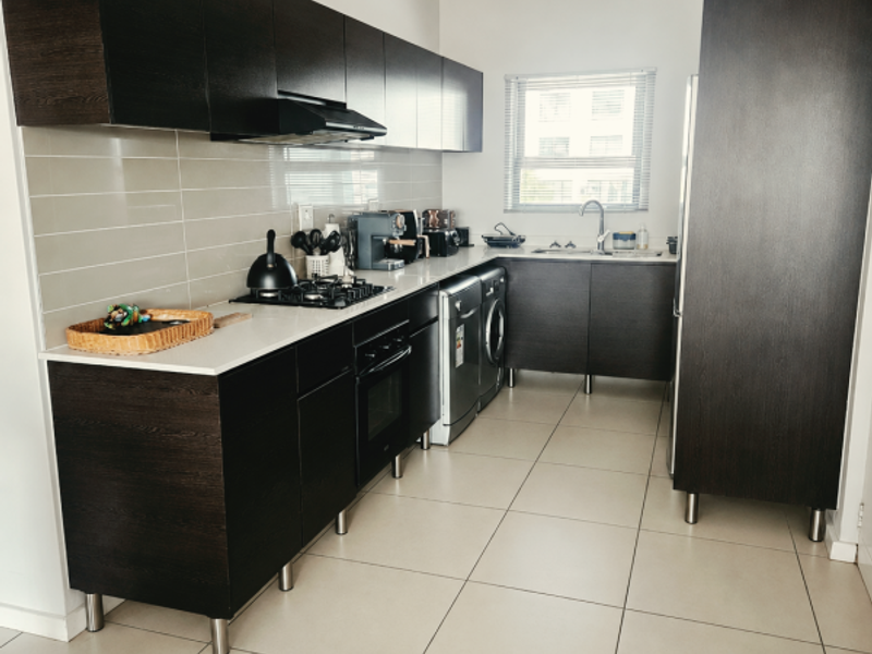 Modern kitchen featuring dark wood cabinetry, built-in oven, gas hob, extractor fan, and tiled flooring with integrated space for laundry appliances.