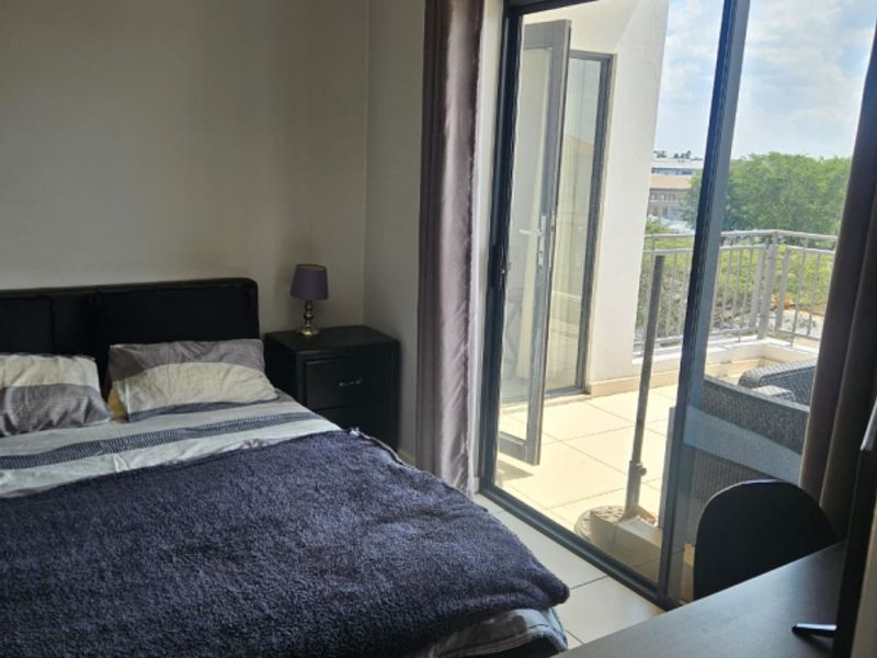 A well-lit bedroom featuring tiled flooring and a large sliding glass door providing direct access to a private balcony.