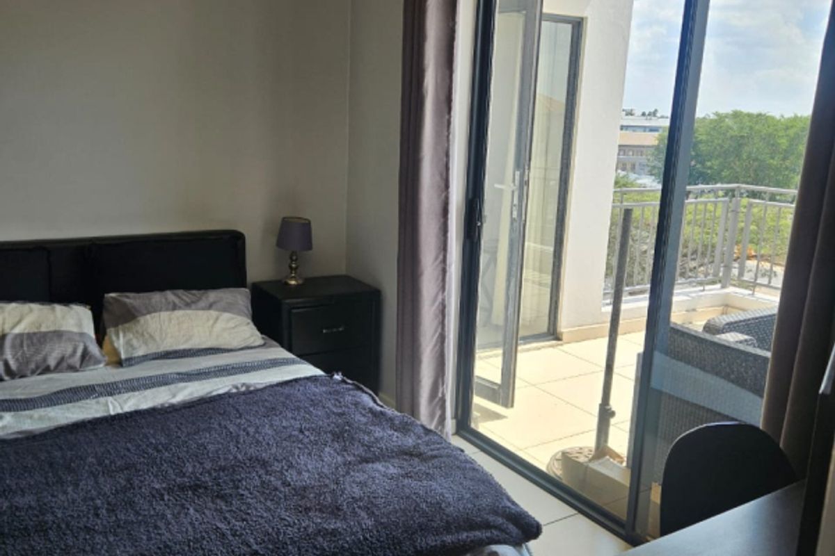 A well-lit bedroom featuring tiled flooring and a large sliding glass door providing direct access to a private balcony.