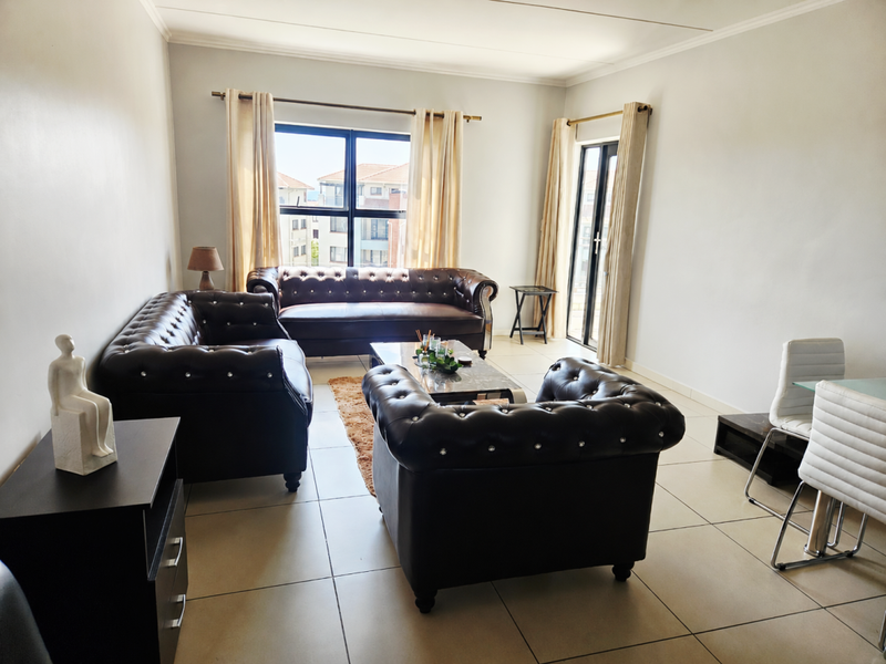 A bright and spacious living room featuring neutral tiled flooring, large windows, and a sliding glass door providing access to the exterior.