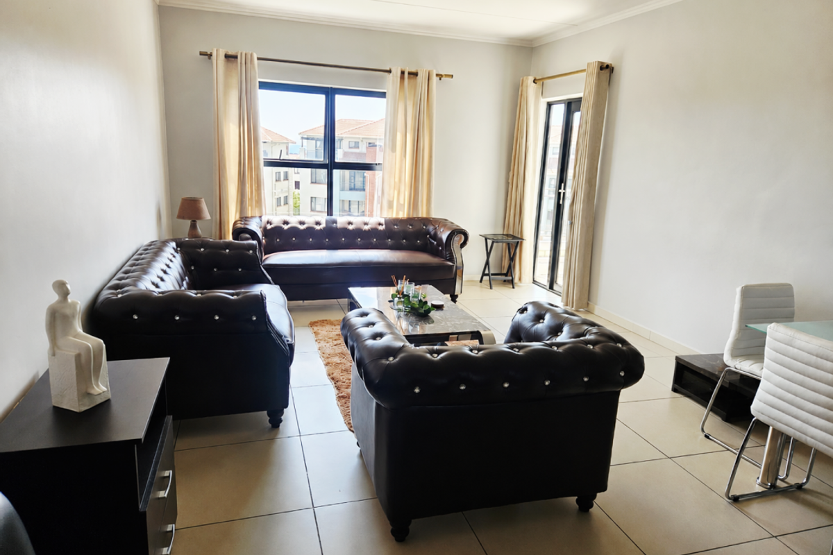 A bright and spacious living room featuring neutral tiled flooring, large windows, and a sliding glass door providing access to the exterior.
