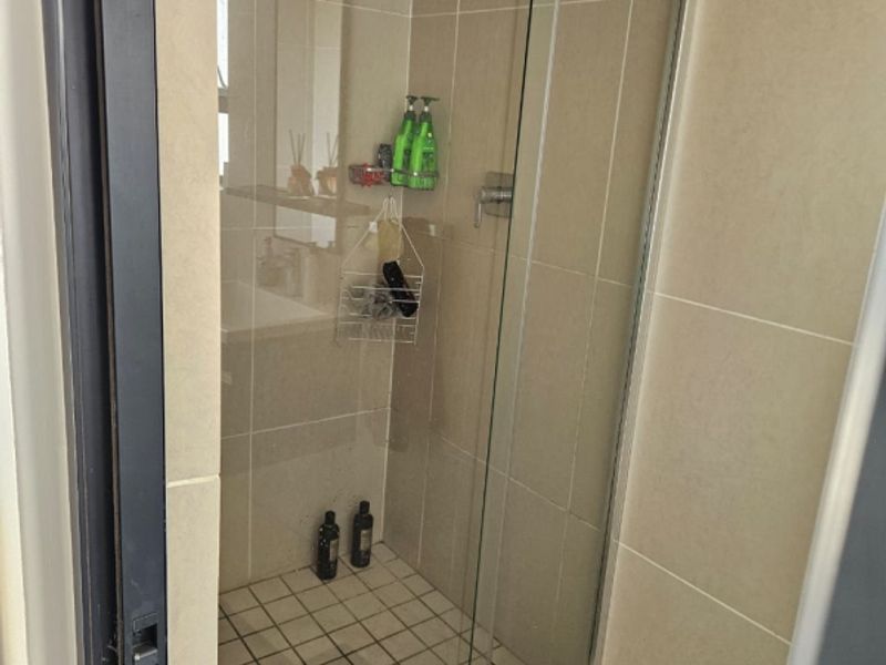 A functional bathroom shower featuring a glass sliding door, neutral wall tiling, and a tiled shower base.