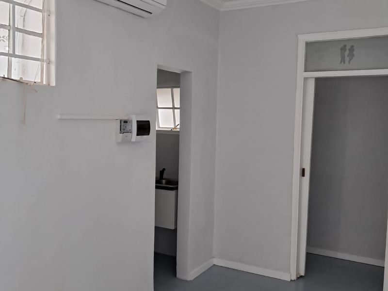 A clean, empty living area featuring neutral walls, coving, an air conditioning unit, and access to adjacent rooms.