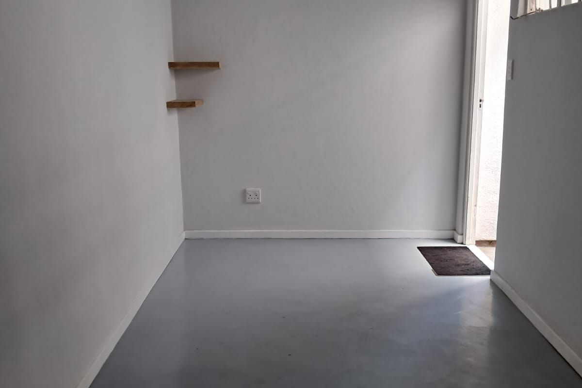 A clean, empty living space featuring neutral walls, grey painted flooring, floating shelves, and direct access to an exterior area.