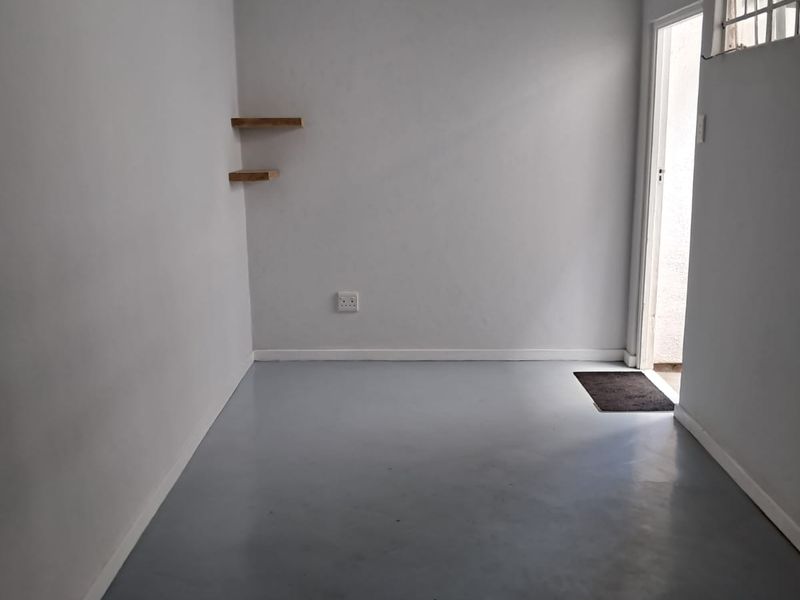 A clean, empty living space featuring neutral walls, grey painted flooring, floating shelves, and direct access to an exterior area.
