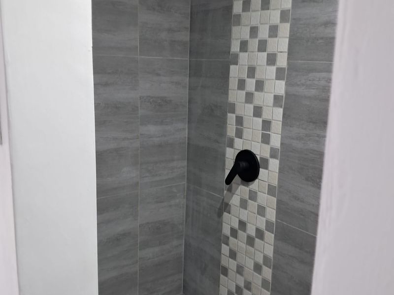 A modern, well-maintained shower enclosure featuring contemporary grey tiling, a decorative mosaic accent strip, and sleek black fixtures.
