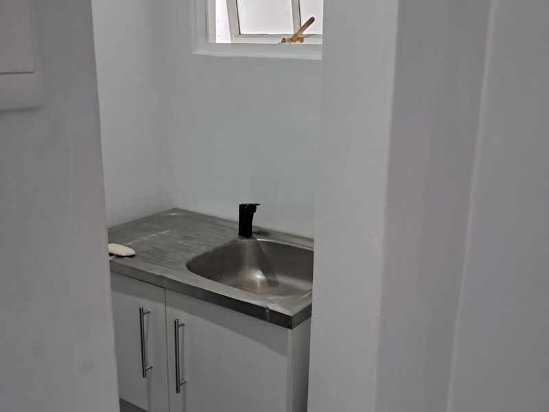 A compact and functional scullery area featuring a stainless steel sink, modern faucet, and clean white cabinetry.