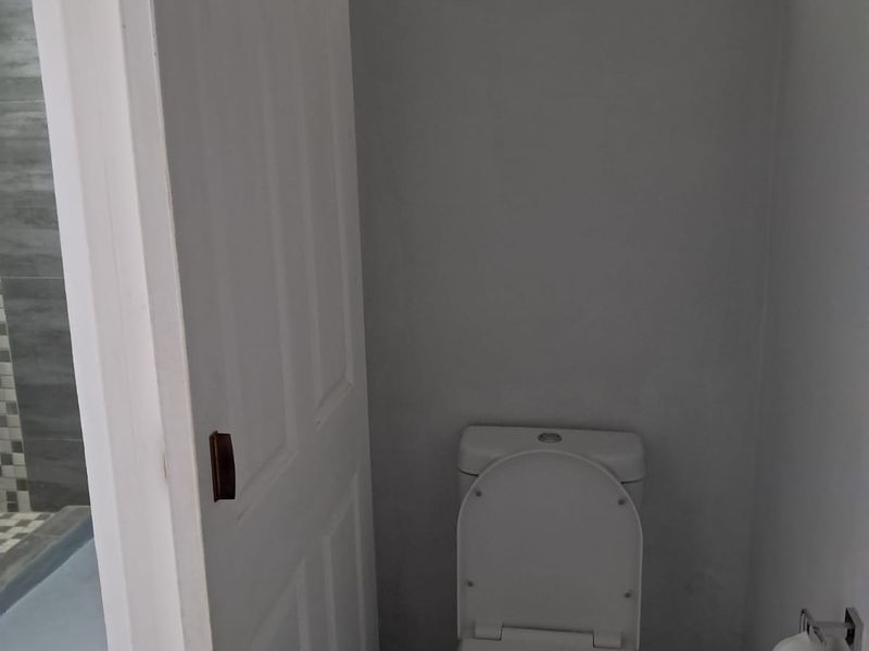 A compact, functional bathroom featuring a standard toilet, tiled flooring, and a small obscured glass window for natural light and ventilation.